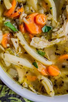 a white bowl filled with chicken noodle soup on top of a green table cloth