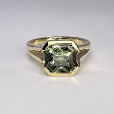 a ring with a green stone in the center on a white surface, it is gold