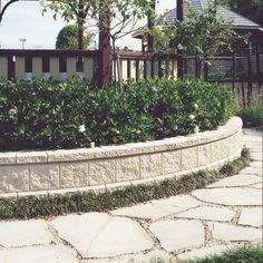 a stone garden wall next to a building with a clock on it's side