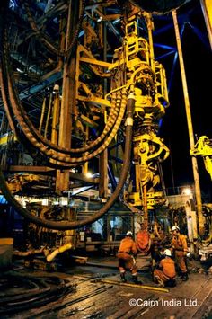 workers are working on an industrial machine in the middle of a large factory area at night