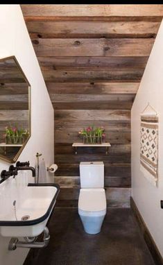 a white toilet sitting in a bathroom next to a sink and wooden planks on the wall