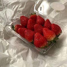 a plastic container filled with strawberries on top of a white sheet covered tablecloth