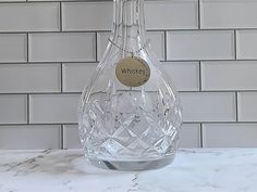 a glass bottle with a label on it sitting on a marble counter top in front of a white brick wall