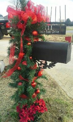 a mailbox decorated with christmas decorations and red bows is sitting in the grass next to a tree