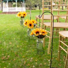 sunflowers in mason jars are hanging from the back of chairs at an outdoor ceremony