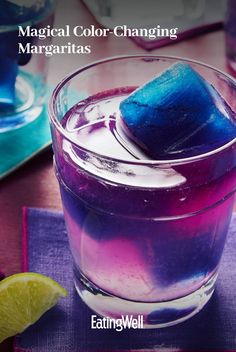 a purple and blue drink sitting on top of a table next to a slice of lemon