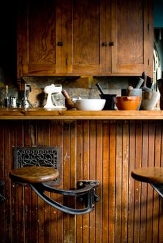 two wooden stools sitting next to each other in front of a bar with bowls and cups on it