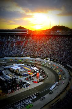 the sun is setting over a race track with cars driving on it and spectators in the stands