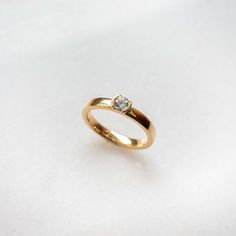 a yellow gold ring with a single diamond on the top, sitting on a white surface