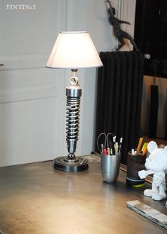 a lamp sitting on top of a wooden table next to a cup and pen holder