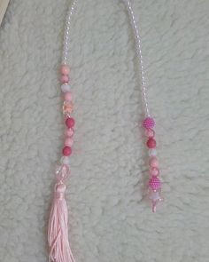 two necklaces with pink beads and tassels on a white surface next to a pair of scissors