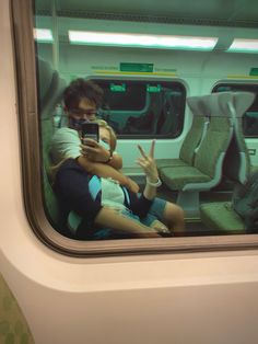 two people sitting on a train looking at their cell phones while they are holding each other