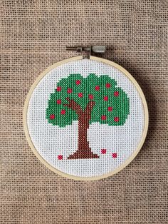 a cross stitch tree with red berries on it's green leafy branches is hanging from a wooden hoop