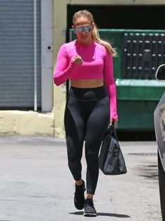 a woman in pink top and black leggings walking down the street with her hand on her hip