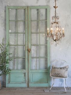 an old green door with glass panels and a chandelier hanging from the ceiling