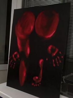 a black and red painting on a white table next to a window with blinds in it