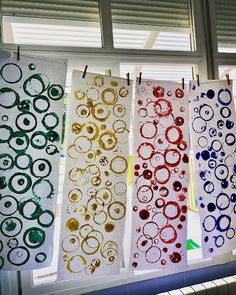 four different colored circles are hanging on a line in front of a window with blinds