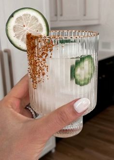 a person holding up a glass with cucumber and limes on the rim