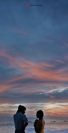 two people standing next to each other on a beach at sunset with clouds in the sky