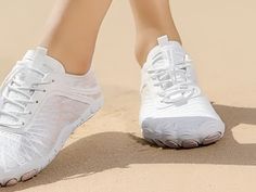 a woman's feet in white tennis shoes on the sand