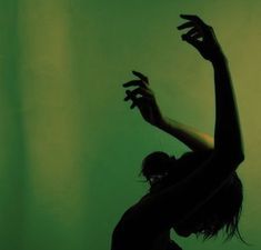 a woman standing in front of a green wall holding her hands up to the side