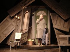 an old man standing on stage in front of a house