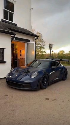 a blue sports car parked in front of a white house with an open garage door