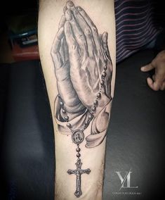 a black and white tattoo of a praying hands with a rosary on it's arm