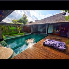 an outdoor swimming pool with wooden decking and green plants on the other side, surrounded by greenery