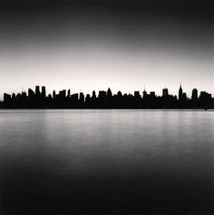 a black and white photo of a cityscape with the water reflecting it's skyline