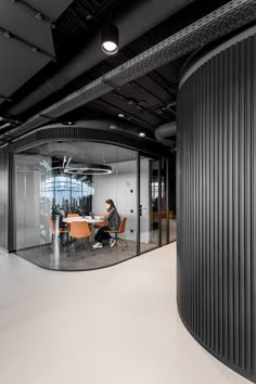 a woman is sitting at a table in an office with black walls and round glass partitions