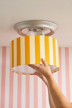 a woman is holding up a yellow and white striped lamp shade in front of her face