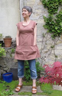 a woman standing in front of a stone wall with potted plants on the side