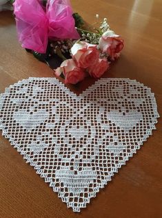 a heart shaped doily sitting on top of a wooden table next to pink flowers