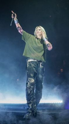 a male in a green shirt and black pants on stage with his arms out to the side