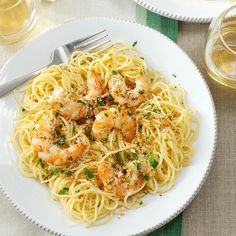 pasta with shrimp and parmesan cheese on a white plate next to a glass of wine