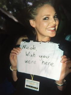 a woman holding up a sign that says nicole, wish you were here