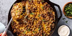 a large skillet filled with taco meat and cheese next to some sour cream