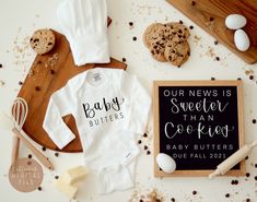 baby onesuits and cookies are laid out on a table next to a sign