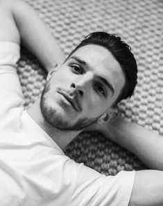 a black and white photo of a man laying on a bed with his hands behind his head