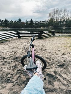 a person sitting on top of a bike in the middle of a dirt field next to a fence