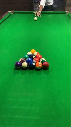 a pool table with several balls on it and a man in white shirt leaning over the edge