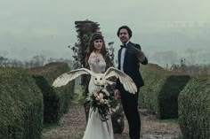 a man and woman standing next to each other in front of hedges with an owl on it's back