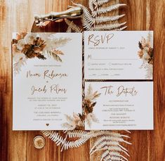 the wedding stationery is laid out on a wooden table with ferns and pine cones