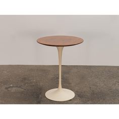 an oval table with a wooden top and white base on a concrete floor in front of a wall