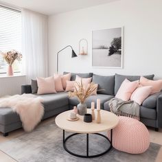 a living room with grey couches and pink pillows on the floor, white walls