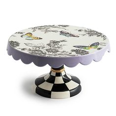 a decorative cake plate with flowers and butterflies on the top, sitting on a black and white checkerboard pedestal