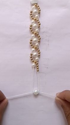 two hands are working on a beaded bracelet with pearls and gold beads hanging from it