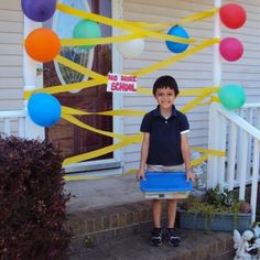 a young boy is standing on the front porch with balloons and streamers around him