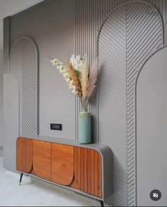 a vase with some flowers sitting on top of a wooden cabinet next to a wall